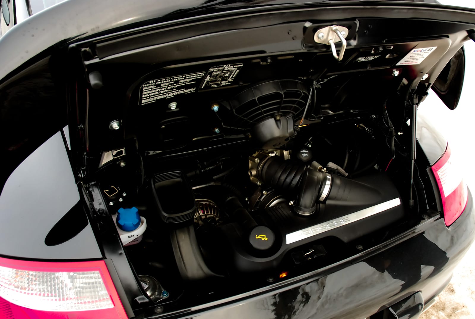 Open engine lid of a black Porsche 911 (997) Carrera showing the flat-six engine and intake